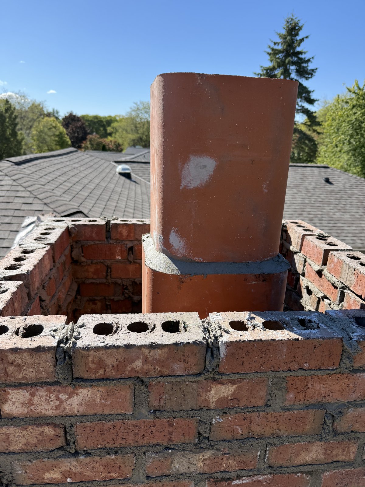 Greenfield chimney code build-up mid-construction with stacked terracotta flue liner.