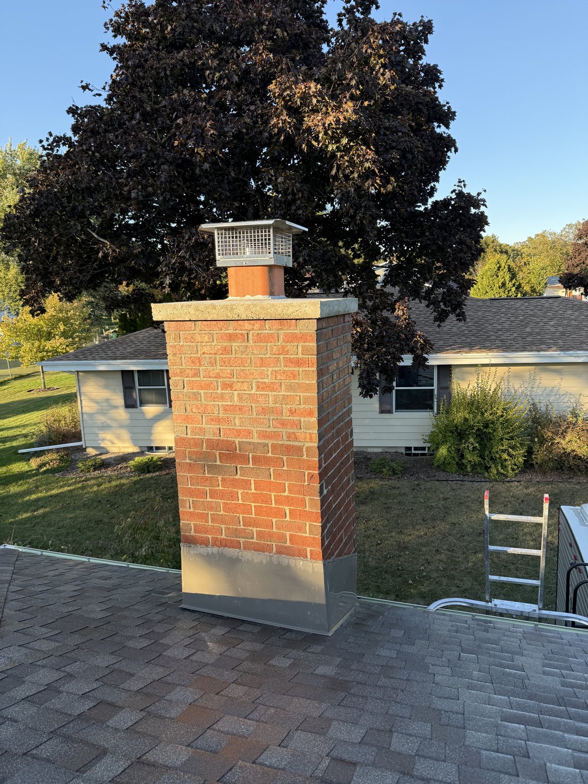 Completed Greenfield chimney code build-up with new brick, crown, and stainless spark-arrestor cap for a wood-fueled fireplace.