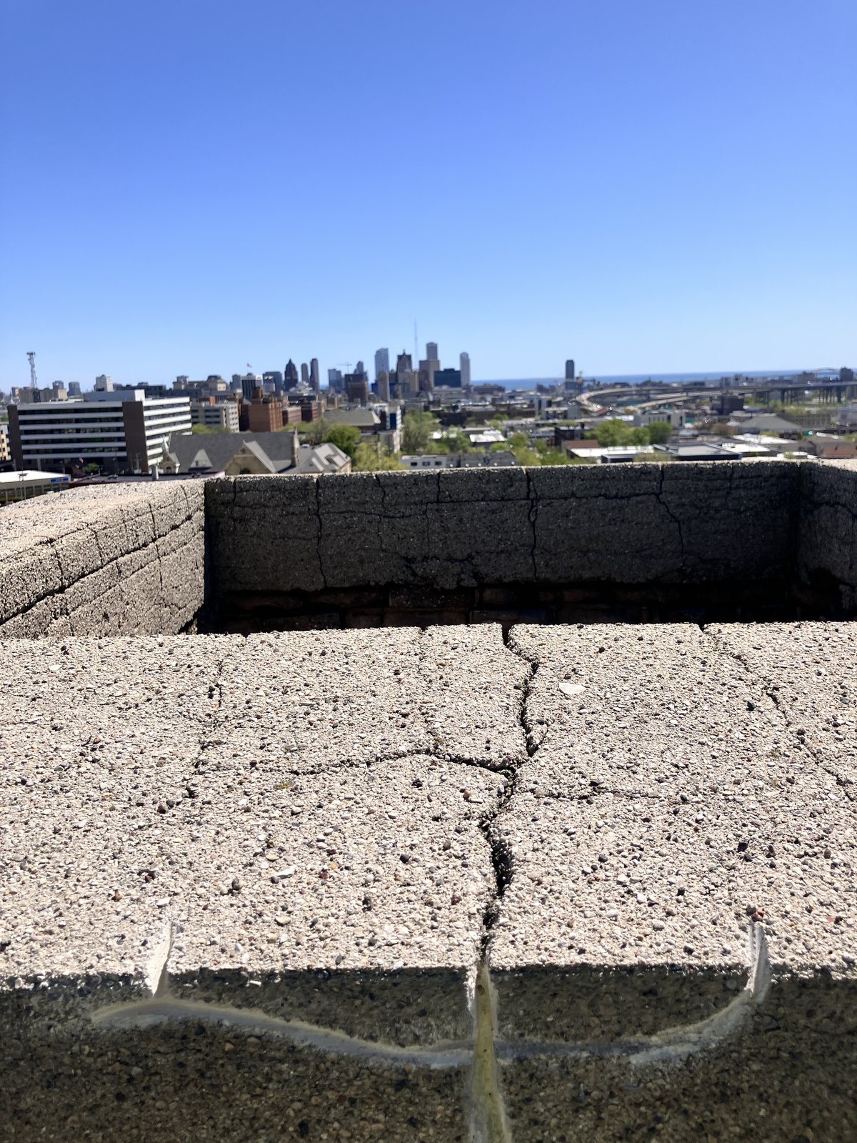 Cracked commercial parapet masonry with Milwaukee skyline beyond.