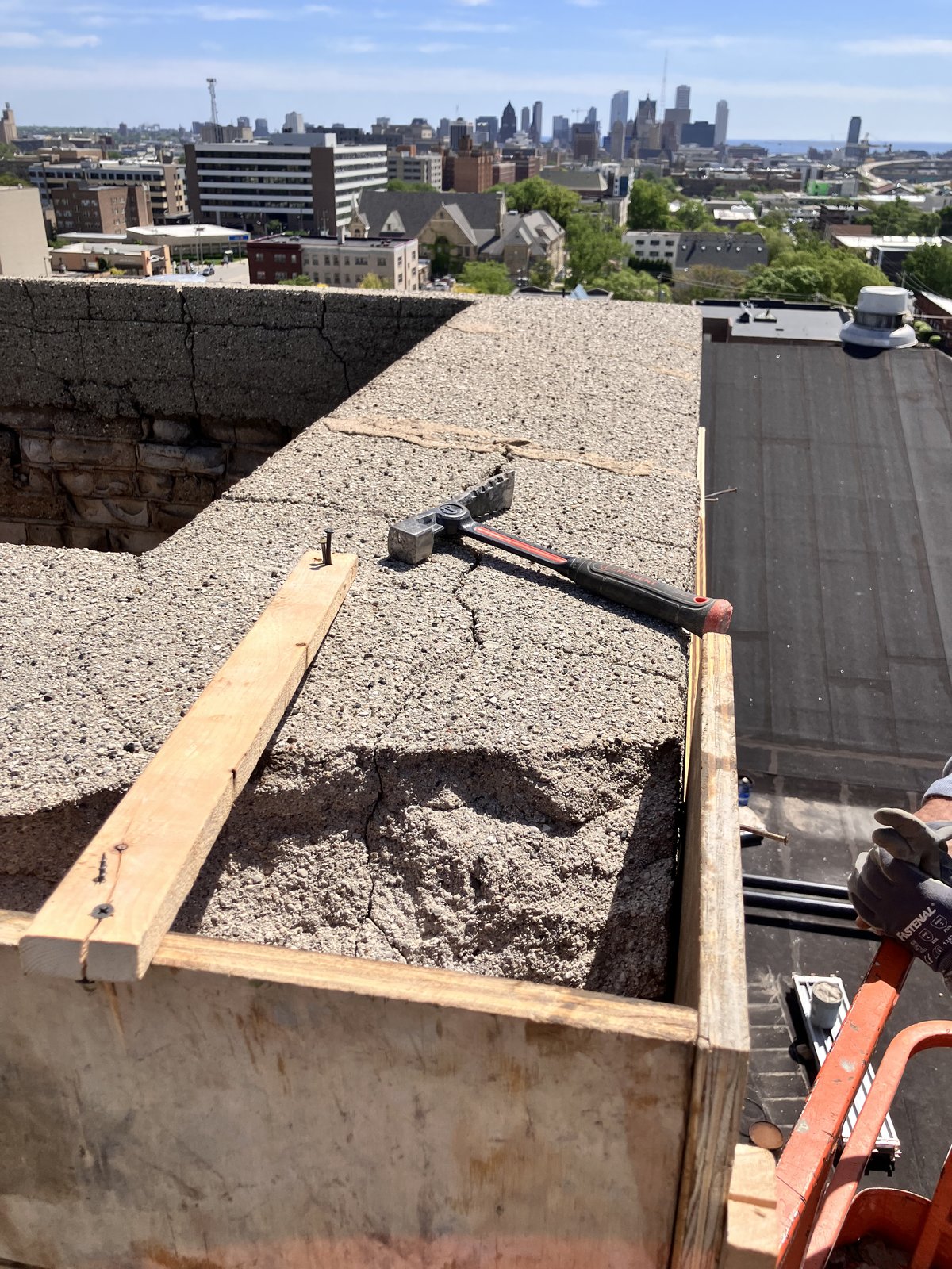 Masonry formwork and hammer on a weathered rooftop parapet overlooking the Milwaukee skyline.